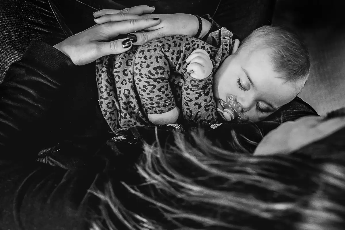 Slapende baby in armen van moeder van bovenaf gefotografeerd.