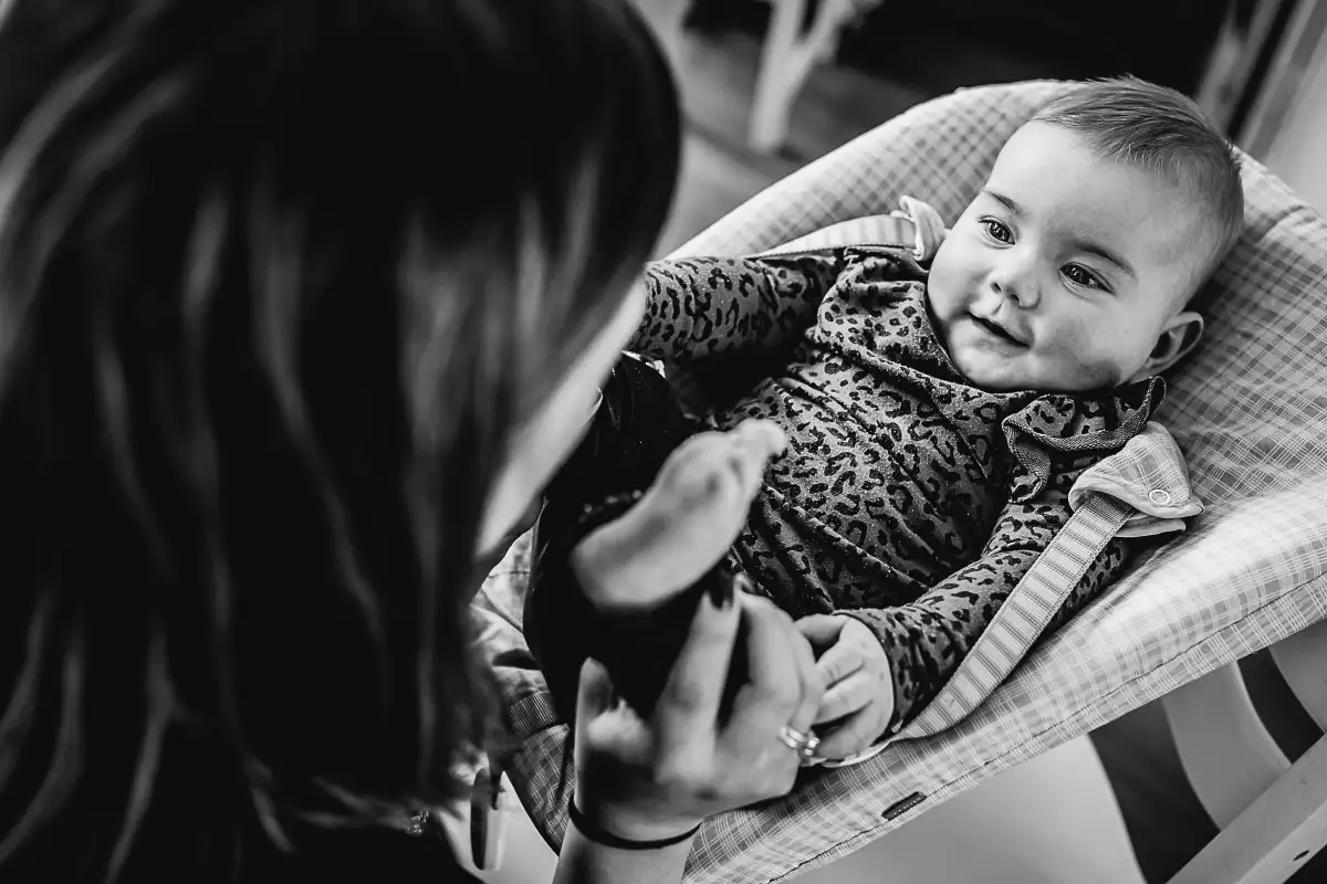 Baby in wipstoel lacht naar haar moeder.