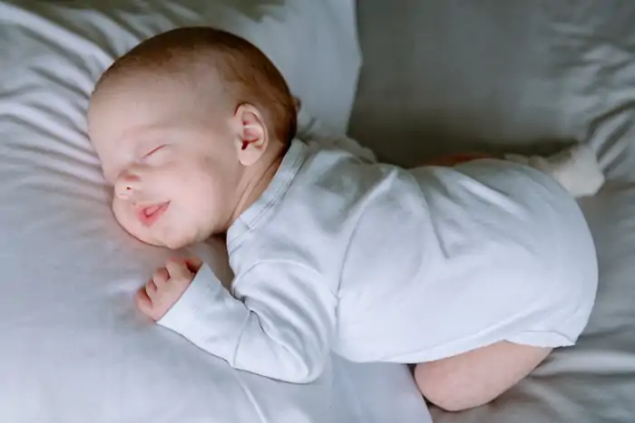 Baby in wit rompertje lacht een beetje tijdens een shoot