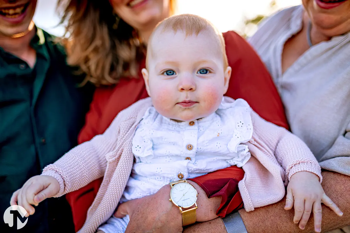 Baby gedragen door haar moeder kijkt recht in de camera tijdens een fotosessie.