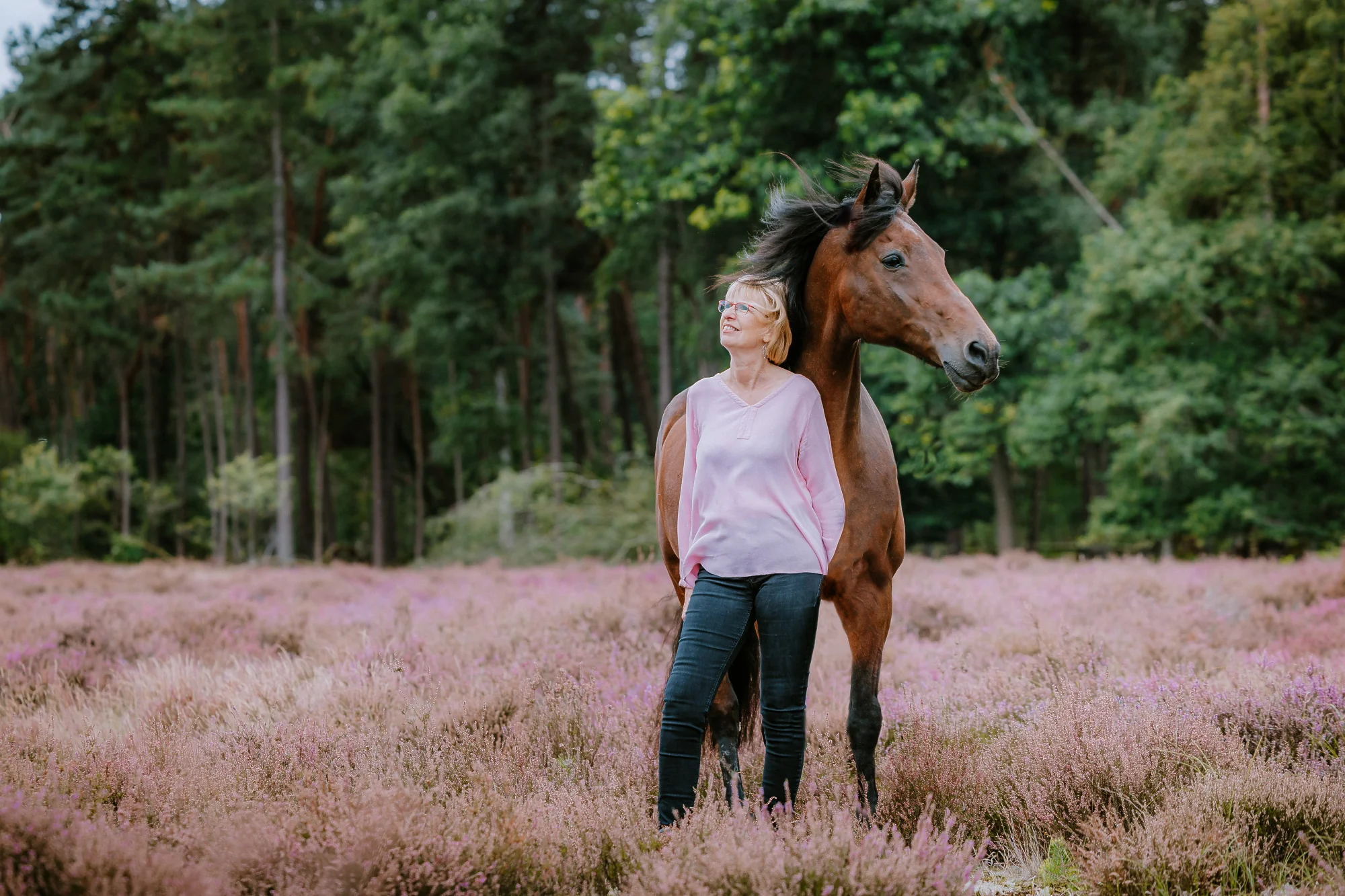 vrouw staat voor paard en beide kijken een andere richting op in de heide