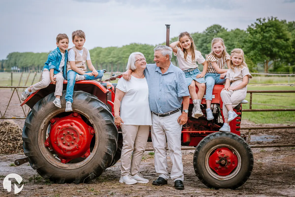 Familiefoto met opa en oma met hun kleinkinderen bij een rode tractor op hun boerderij.