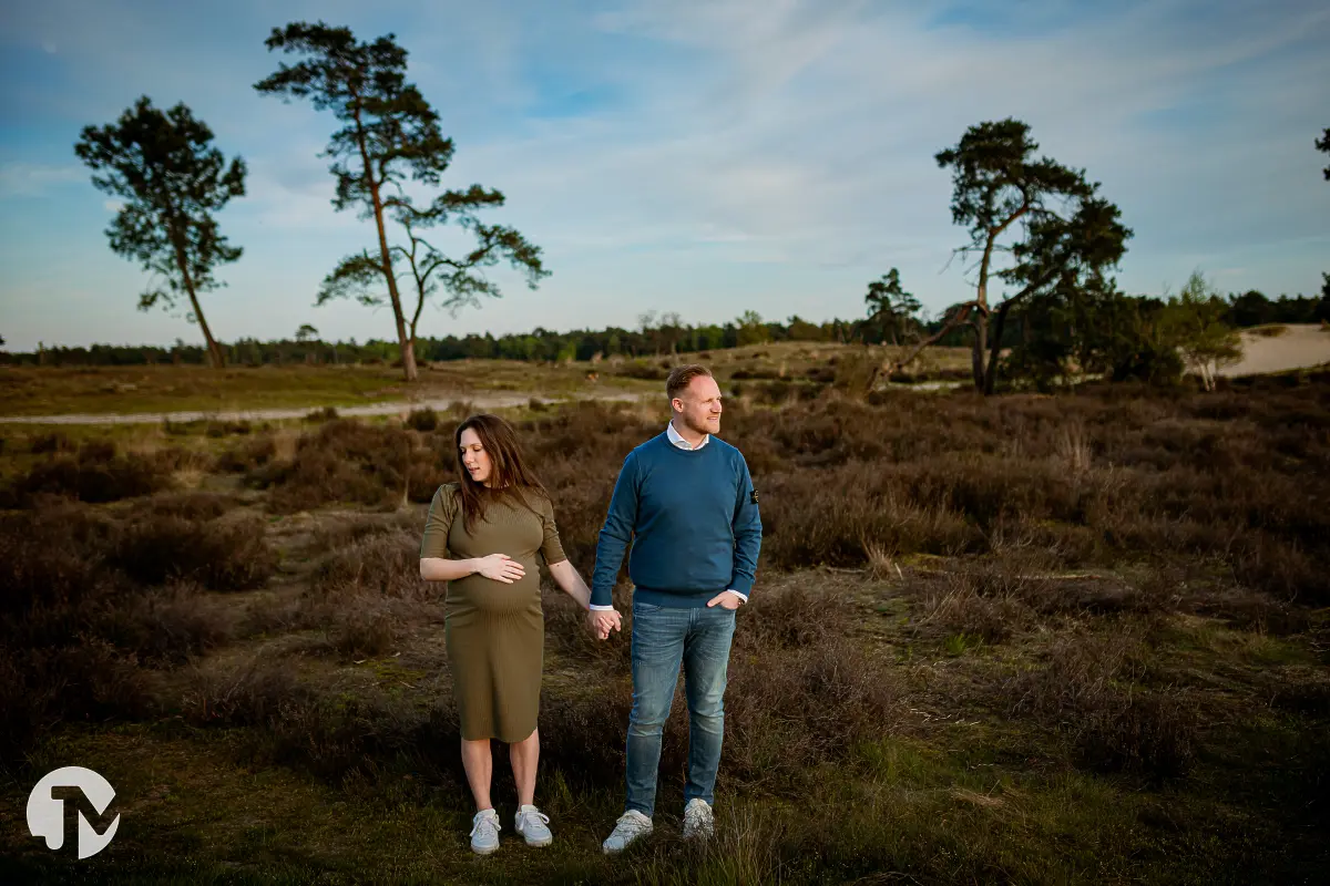 Warme foto van een stel dat een kleintje verwacht lopend door de Loonse Duinen