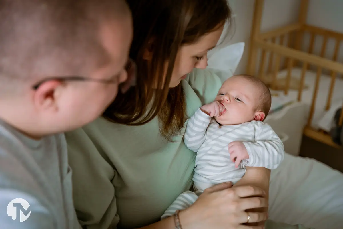 Jong gezin geniet van hun baby op bed tijdens een niet geposeerde baby fotoshoot.
