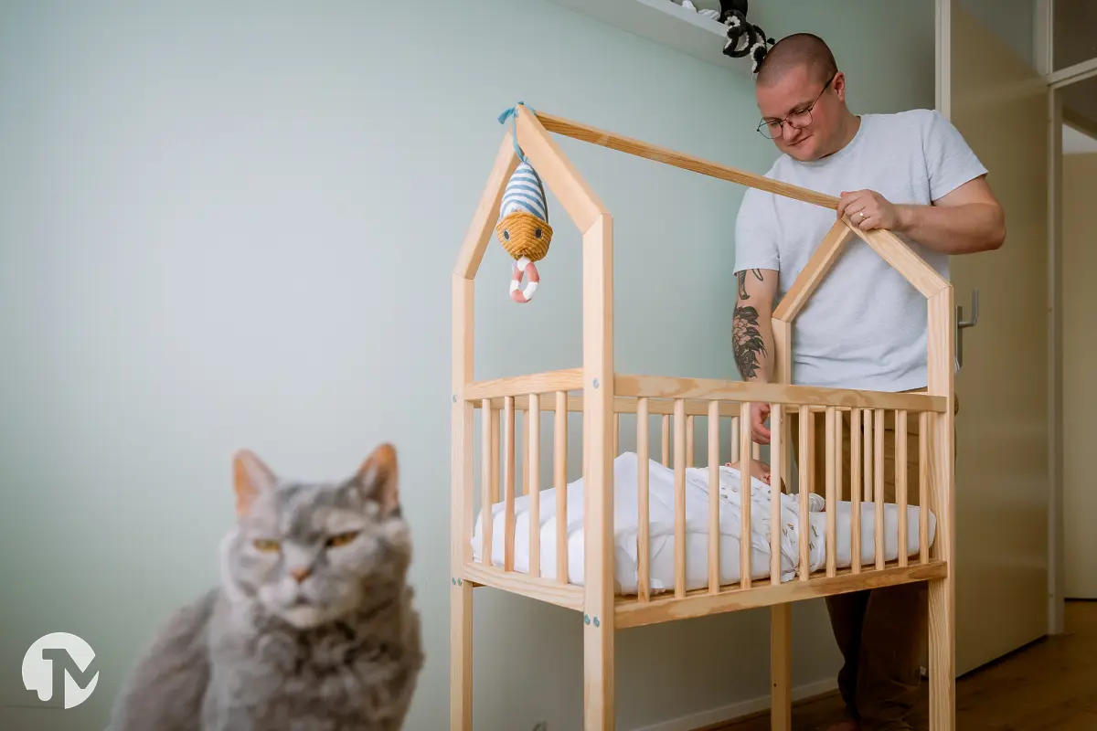 Vader legt baby op kinderkamer in het wiegje, hun kat kijkt ontspannen op de voorgrond weg