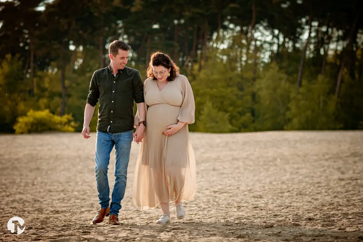 Zwangere vrouw met haar partner lopen door de zandvlakte tijdens zwangerschapsshoot.