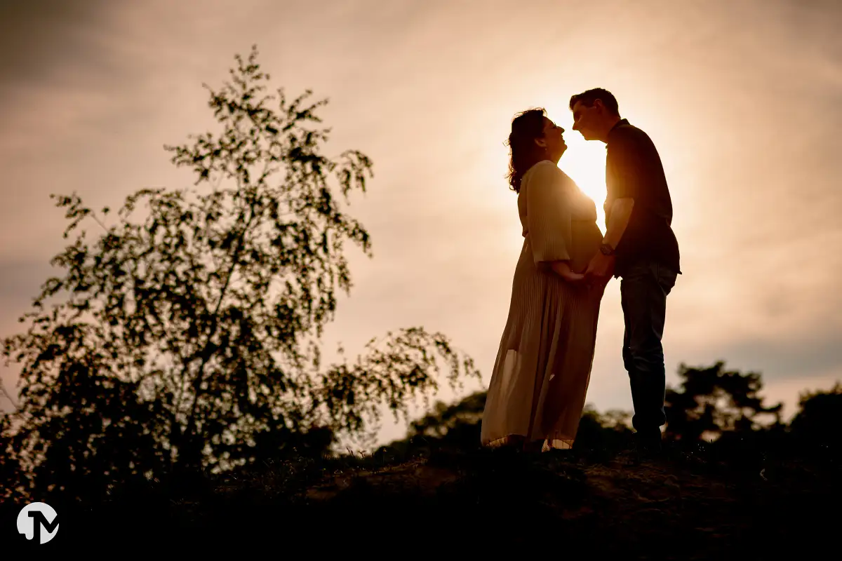 Silhouette van zwangere vrouw en man tijdens shoot in het golden hour.