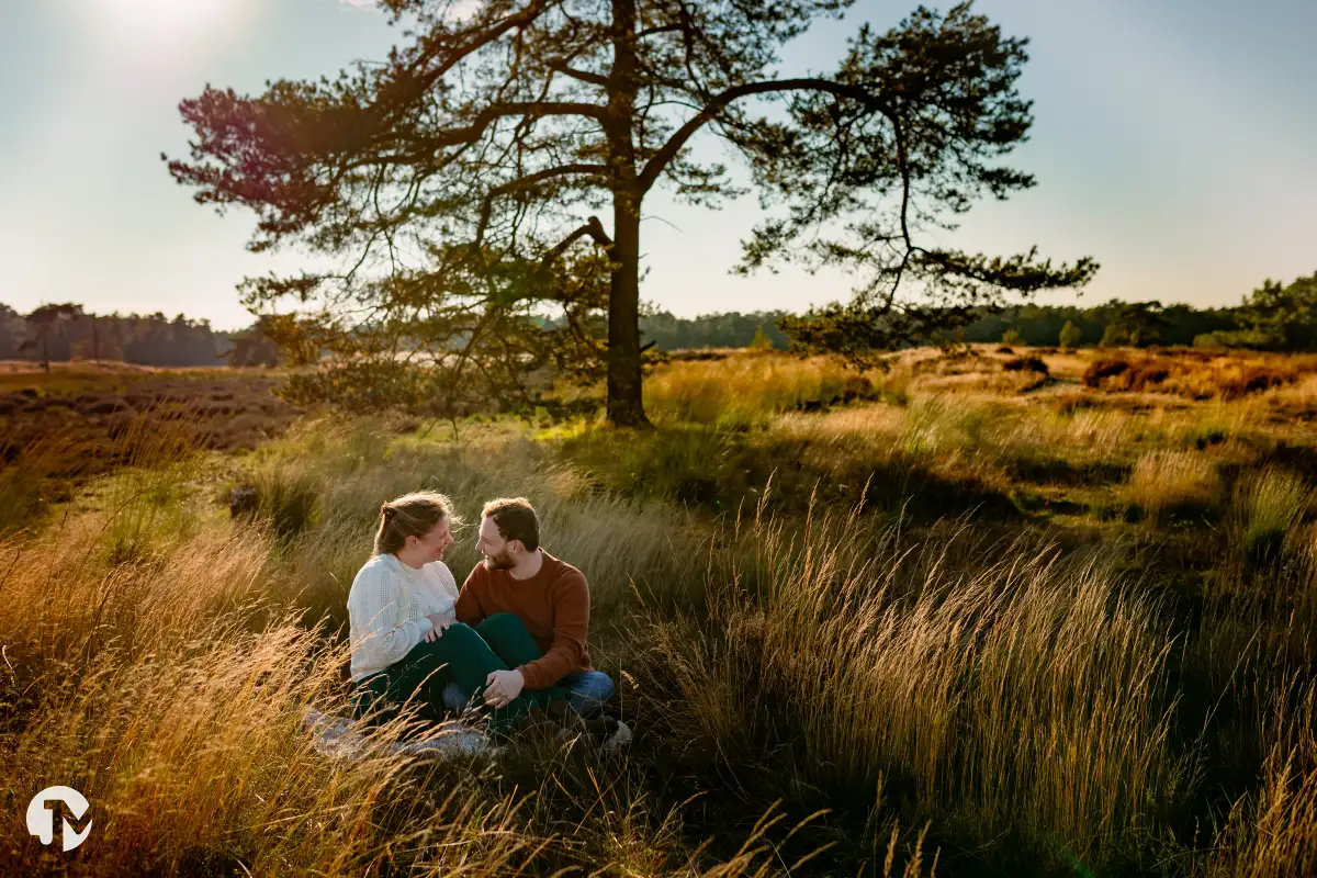 Man en vrouw in het gebied van de Loonse duinen zitten in het hoge gras bij een boom.