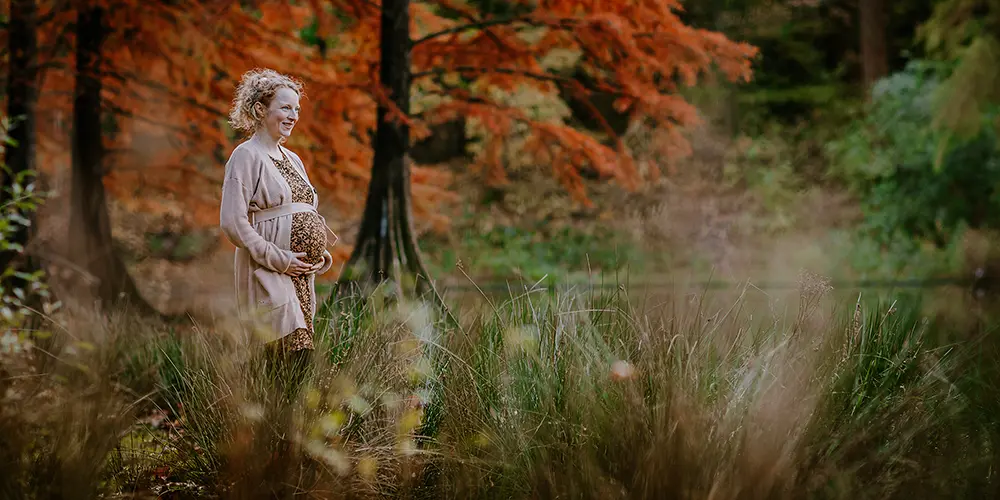 Zwangere vrouw staat in de natuur tijdens een herfst zwangerschapsshoot in het Wandelbos in Tilburg